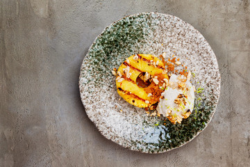 Plate of smoked coconut milk icecream served with pineapple and puffed rice at concrete table background with copyspace.