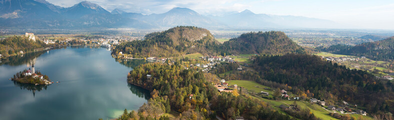 Aerial panorama of lake Bled and green valley with houses and forest in early morning