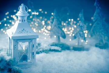 Vintage Christmas lantern with burning candle in grey blue snow landscape with magic bokeh lights -...