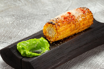 Closeup image of grilled sweet corn with salt served with green sauce at wooden board at concrete table background.
