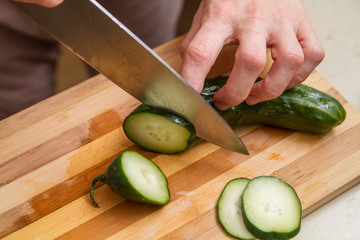 Chef slicing a fresh cucumber in the kitchen on a bamboo kitchen board