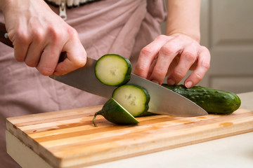 Female Chef Slices a fresh cucumber with a sharp knife on a kitchen table