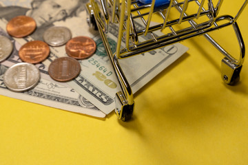 Rear wheels souvenir stroller for shopping and US money. Yellow background. Shopping online or offline. Concept of discounts and sales, business or inflation, consumer basket and financial crisis.