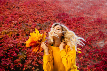 Portrait of cheerful young woman with autumn leafs in front of foliage making selfie