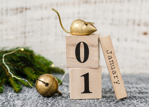 Chinese New Year 2020. Date January 1 on a wooden calendar with metal rat and christmas bell and twigs of a Christmas tree on agrey background. New Year of the rat.