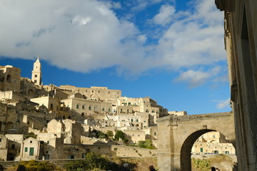 Panorama of the Sassi of Matera with houses in tuff stone. Church with bell tower and stone arch at dawn with sky and clouds..