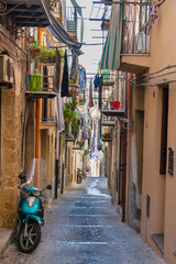 Narrow italian street with balconies and scooters in summertime