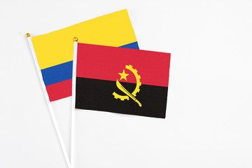 Angola and Colombia stick flags on white background. High quality fabric, miniature national flag. Peaceful global concept.White floor for copy space.