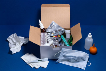 Cardboard box with medical supplies on dark blue background. Pills in blister packs. Cold and flu season