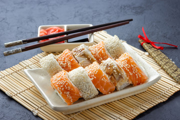 Sushi roll, chopsticks, soy sauce, ginger and bamboo mat.