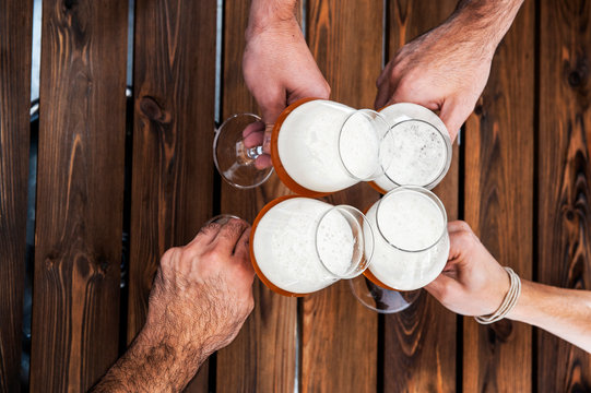 Top view of four hands with beers cheering and having fun together - wood table