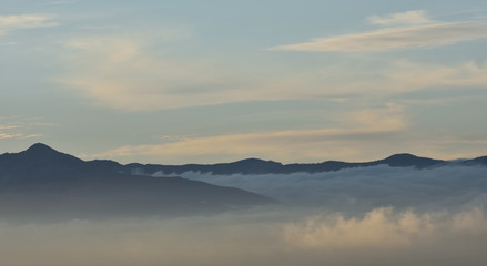 Sea of clouds at sunrise between mountains with some lenticular cloud in the sky