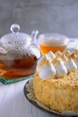 Cake beautifully decorated with whipped protein peaks next to a glass teapot and a cup of tea are ready for tea drinking, vertical orientation