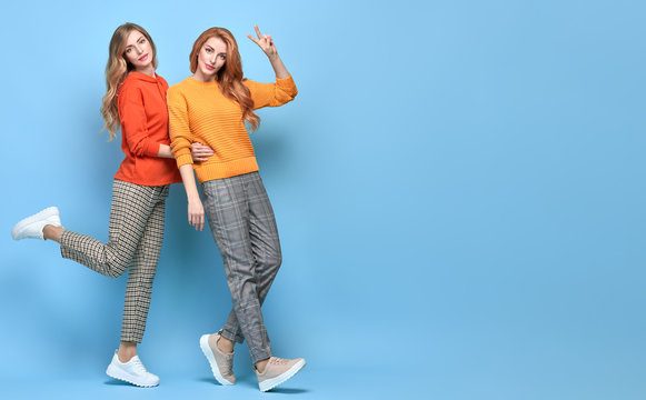Two Lovable embracing fashionable woman sisters dance in Trendy orange outfit. Carefree beautiful funny stylish friends laughing on blue. Happy fashion girl, dancing positive mood, peace sign