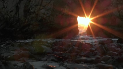A sunstar pierces a coastal monolithic rock creating a natural wonderous oceanic phenomenon as the sun rays align with the keyhole at sunset only one week per year at Big Sur California, USA. 