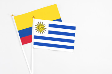 Uruguay and Colombia stick flags on white background. High quality fabric, miniature national flag. Peaceful global concept.White floor for copy space.