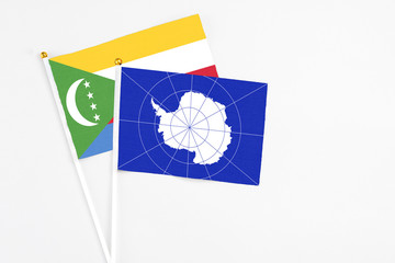 Antarctica and Comoros stick flags on white background. High quality fabric, miniature national flag. Peaceful global concept.White floor for copy space.