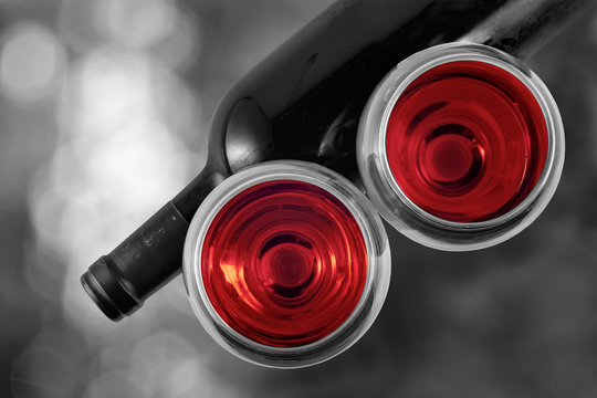  Black and white image of a bottle of wine and a glass of red wine with an accent of red on an abstract background with bokeh effect