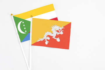 Bhutan and Comoros stick flags on white background. High quality fabric, miniature national flag. Peaceful global concept.White floor for copy space.