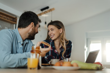 Young smiling couple communicating during breakfast time in the kitchen