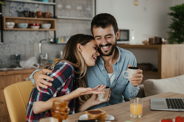 Young cheerful couple having fun during breakfast time in the kitchen