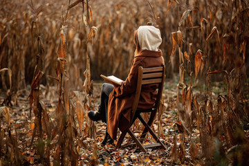 Style woman with book sitting on chair on corn field in autumn time season