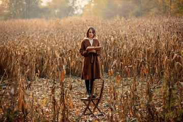 Style woman with book stay on chair on corn field in autumn time season