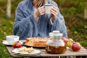 woman holding tea cup and sitting near table with apple pie in garden