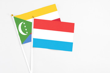 Luxembourg and Comoros stick flags on white background. High quality fabric, miniature national flag. Peaceful global concept.White floor for copy space.