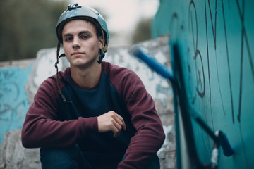 Professional young sportsman cyclist portrait with bmx bike and helmet at skatepark with bmx graffiti