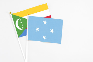 Micronesia and Comoros stick flags on white background. High quality fabric, miniature national flag. Peaceful global concept.White floor for copy space.
