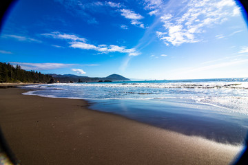 Pacific ocean photography effect, clear water, huge sandy beach, dramatic blue sky and mountains in background on US route 1 California, sunlight and sunbeam effect