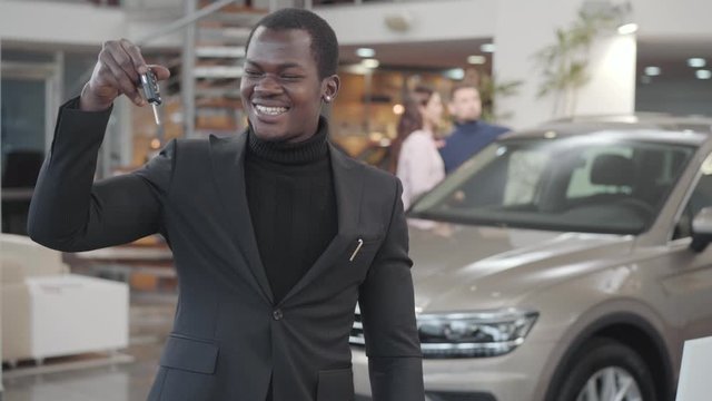 Confident African American Man Coming Up To Camera, Showing Car Keys From New Automobile And Gesturing Yes. Satisfied Businessman In Black Suit Purchasing Vehicle In Car Dealership. Car Business.