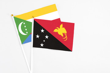 Papua New Guinea and Comoros stick flags on white background. High quality fabric, miniature national flag. Peaceful global concept.White floor for copy space.