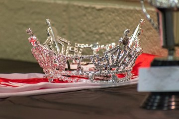 A lone tiara, sash, and trophy sit to be presented to the winner.