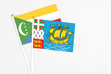 Saint Pierre And Miquelon and Comoros stick flags on white background. High quality fabric, miniature national flag. Peaceful global concept.White floor for copy space.