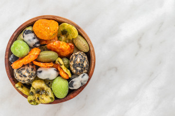 Japanese hot snacks with peanuts, peas and wasabi lie in a brown bowl on a white marble surface on the left, on the right is an empty place