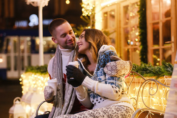 Inbetween Christmas decorations romantic couple enjoying hot drinks while have a date.