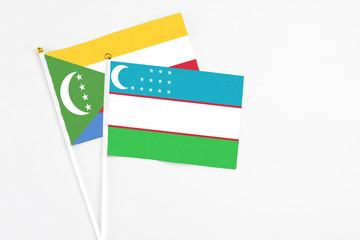 Uzbekistan and Comoros stick flags on white background. High quality fabric, miniature national flag. Peaceful global concept.White floor for copy space.