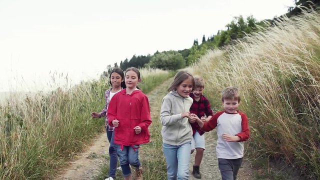 Front view of group of school children running on field trip in nature.