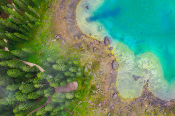 Aerial view of turquoise blue water of lake Carezza in Alps Dolomites. Lago di Karersee near fir tree forest.