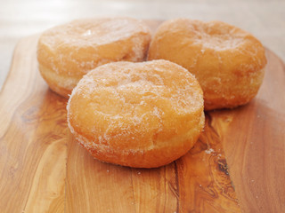 Three fresh tasty doughnuts with sugar coating on a wooden board. Close up.