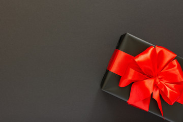 Festive background with gift, black gift box with red ribbon and bow on black background, black...