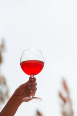A glass of rose wine in hands with drops against the sky.