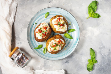 Baked stuffed potatoes with bacon, tomato and cheese on concrete background.