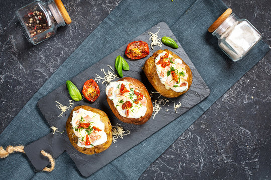 Baked stuffed potatoes with bacon, tomato and cheese on stone background.