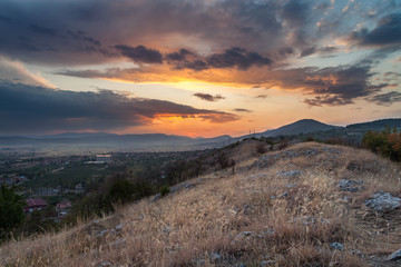Beautiful view from a hill covered by dry grass and rocks on an epic sunset colors of the sky and distant hospital and village