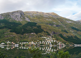 Fototapeta na wymiar View on Ullensvang pitoresque small village over Hardanger Fjord in Norway with small village and colorful houses, forest rocky hill and reflection in bay. Nature travel background. Early autumn day.