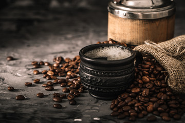 Coffee cup with coffee grinder and coffee beans on dark textured background.
