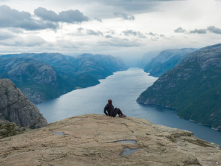 Fototapeta na wymiar Hiker woman admiring view on fjord Lysefjord from Preikestolen massive cliff, famous Norway viewpoint. Moody autumn day. Nature and travel background, vacation and hiking holiday concept.